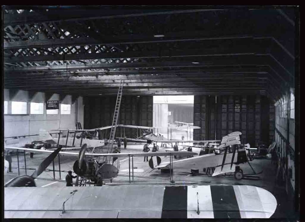 Glass plate negative of various bi-planes being serviced inside a hangar.